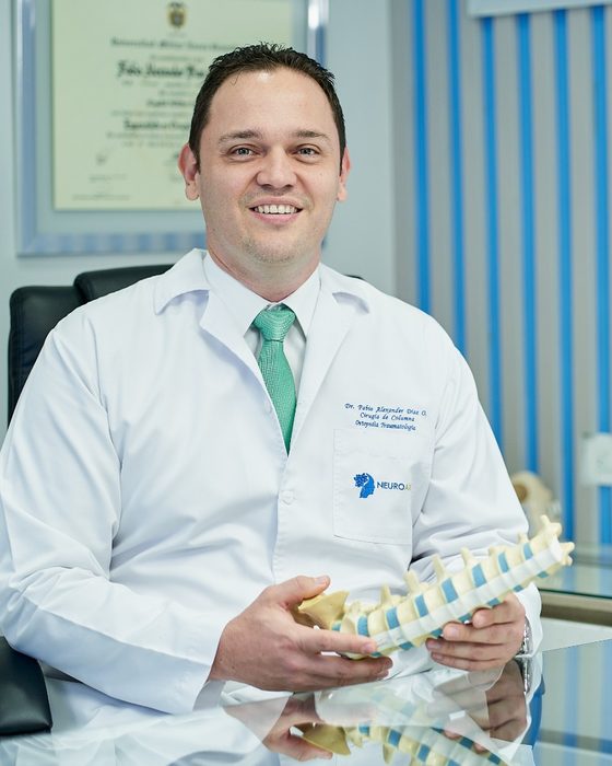 El Dr. Fabio Alexander Díaz Otero en su consultorio, con un modelo de columna lumbar en las manos.